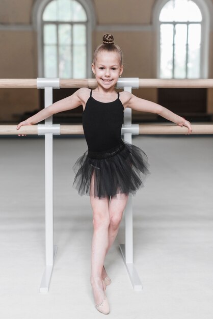 Ragazza sorridente della ballerina in tutu nero che sta davanti alla sbarra