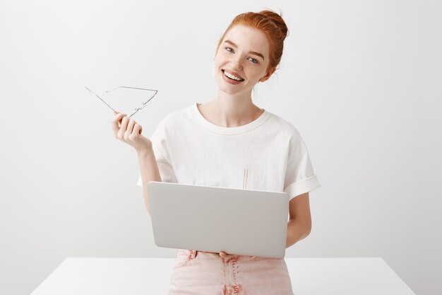 Ragazza sorridente della testarossa che per mezzo del computer portatile e che osserva