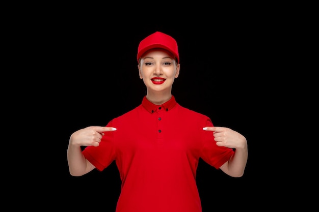 Ragazza sorridente di giorno della camicia rossa che indica se stessa in una camicia da portare del cappuccio rosso con il rossetto