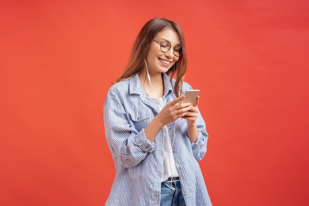 Ragazza sorridente in abbigliamento casual e cuffie che guardano allo schermo del telefono