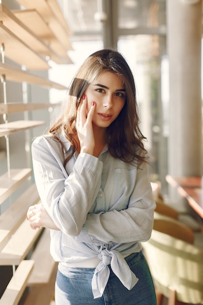 Ragazza sorridente in una camicia blu che sta finestra e posa vicine