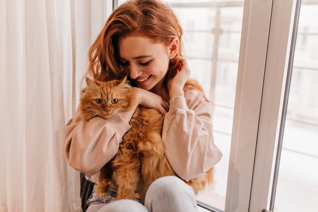 Ragazza sorridente rilassata che gioca con il suo gatto birichino. Tiro al coperto di incredibile lady holding pet.