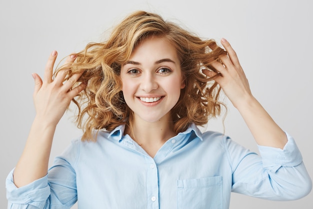 Ragazza sorridente soddisfatta che mostra i capelli ricci dopo il salone di bellezza di parrucchiere