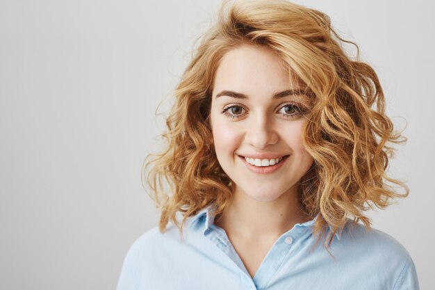 Ragazza sorridente soddisfatta che mostra i capelli ricci dopo il salone di bellezza di parrucchiere