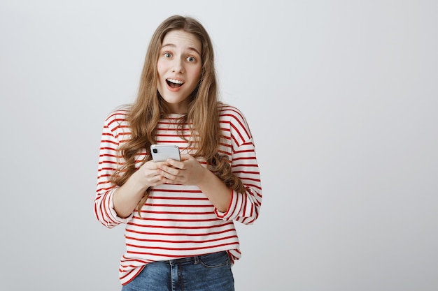 Ragazza sorridente sveglia che tiene smartphone e che sembra soddisfatto