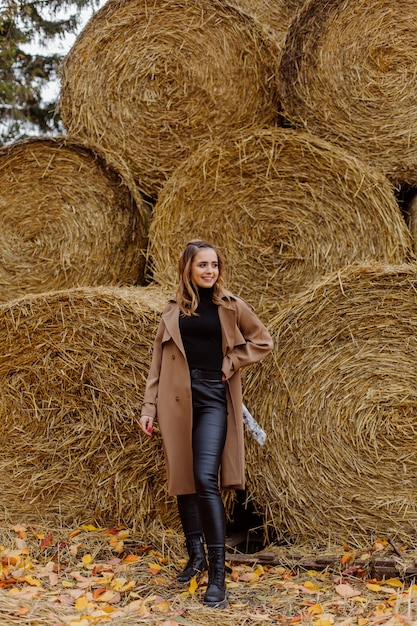 Ragazza sorridente sveglia con il cappello che posa davanti alla balla della paglia del grano