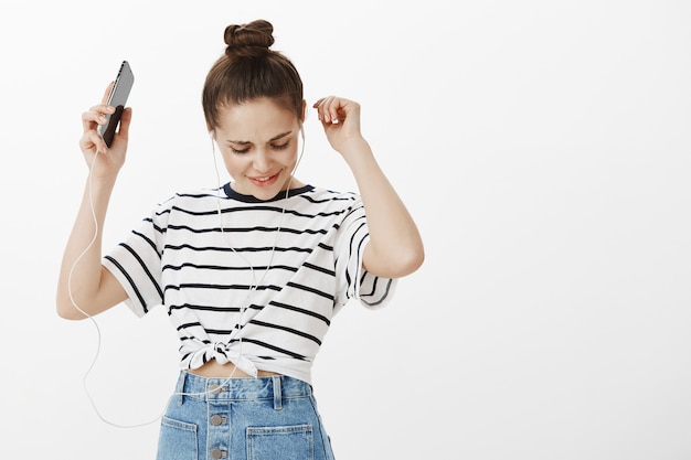 Ragazza spensierata abbastanza caucasica ballando in cuffie con lo smartphone