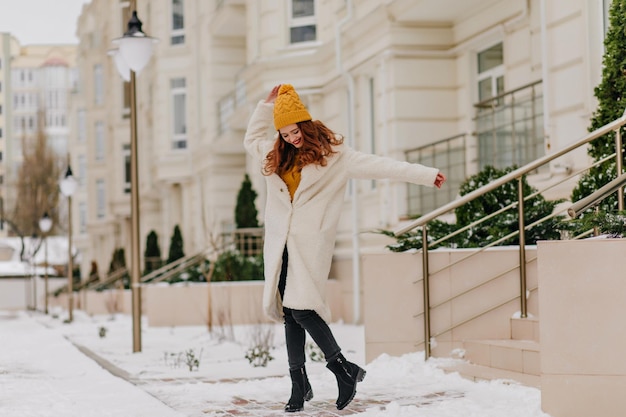 Ragazza spensierata allo zenzero con scarpe nere che ballano nella giornata invernale Foto all'aperto di una donna felice e ben vestita con i capelli lunghi