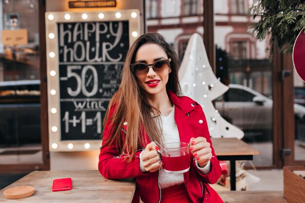 Ragazza spensierata con acconciatura lunga che beve il tè in street cafe