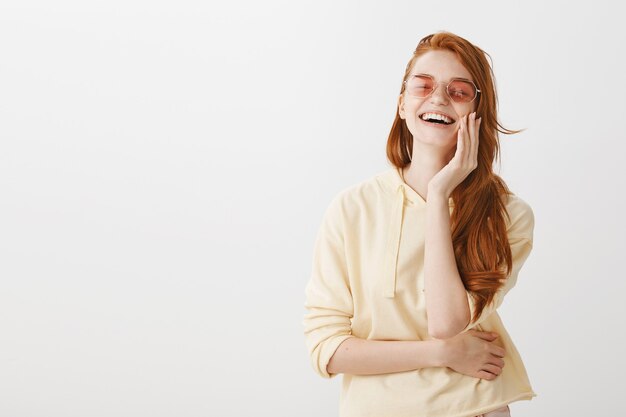 Ragazza spensierata dello zenzero in occhiali da sole che ride dalla felicità