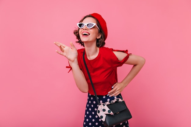 Ragazza spensierata di risata con taglio di capelli corto in posa. Donna bianca francese emotiva in berretto sorridente.