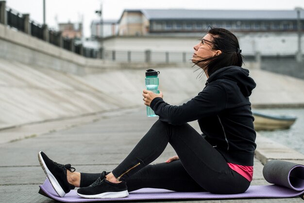 Ragazza sportiva che si siede con la bottiglia di acqua