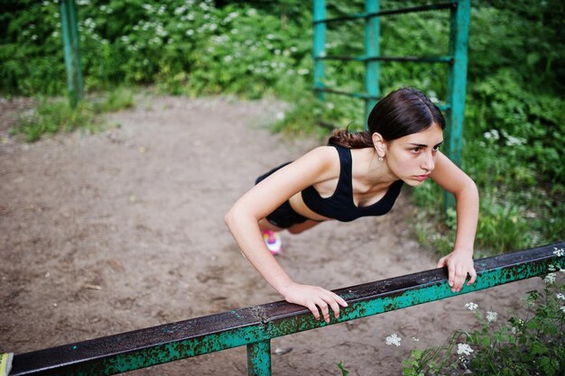 Ragazza sportiva in abbigliamento sportivo che si esercita alla barra orizzontale si esercita in un parco verde e si allena in natura Uno stile di vita sano