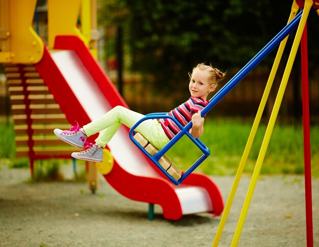 Ragazza su un&#39;altalena nel parco giochi in estate