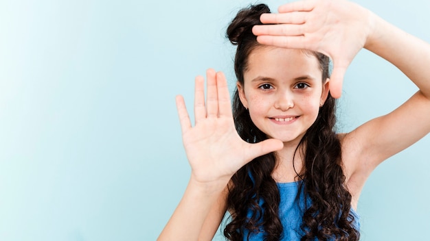 Ragazza sveglia che fa forma della macchina fotografica con le mani