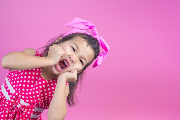 Ragazza sveglia che porta una camicia a strisce rossa, legato un fiocco rosa sulla testa e rosa.