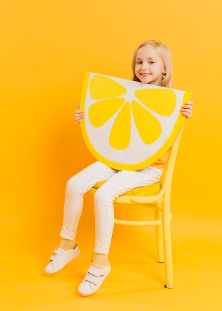 Ragazza sveglia che posa mentre tenendo la decorazione della fetta del limone