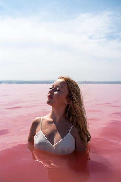 Ragazza sveglia dell'adolescente che porta vestito bianco nell'acqua di un lago rosa stupefacente