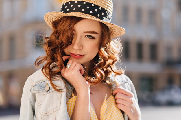 Ragazza sveglia dello zenzero dagli occhi azzurri in posa sulla città di sfocatura. Foto all'aperto di una splendida giovane donna dai capelli rossi in giacca alla moda.