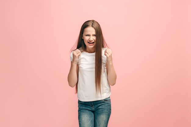 Ragazza teenager arrabbiata che sta sulla parete rosa alla moda dello studio