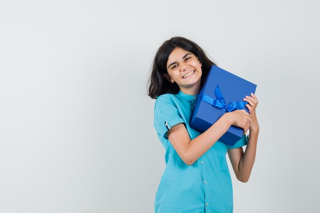 Ragazza teenager che abbraccia la sua scatola attuale in camicia blu e che sembra allegra