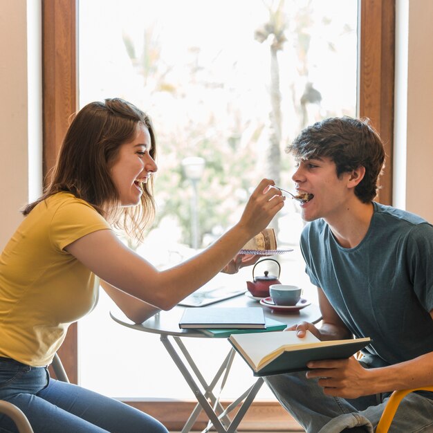 Ragazza teenager che alimenta ragazzo con il dessert in biblioteca