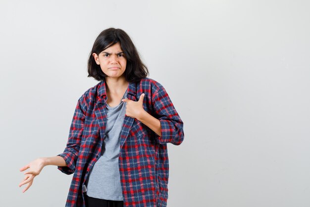 Ragazza teenager che è dispiaciuta per la domanda stupida in camicia a scacchi e sembra lugubre, vista frontale.