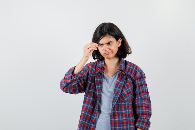 Ragazza teenager che finge di tenere qualcosa di minuscolo in abiti casual e sembra concentrata, vista frontale.