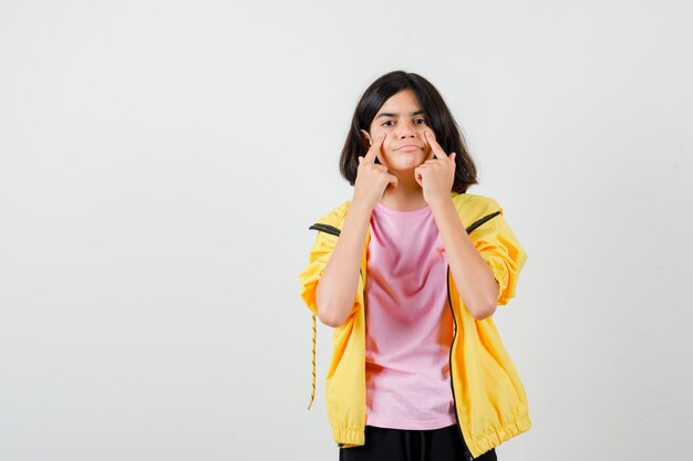 Ragazza teenager che indica i suoi occhi in t-shirt, giacca e guardando focalizzata, vista frontale.