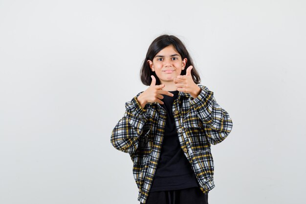 Ragazza teenager che mostra il gesto della pistola in camicia casual e sembra allegra, vista frontale.