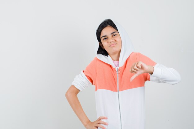 Ragazza teenager che mostra il pollice giù in rivestimento bianco e che sembra scontento.