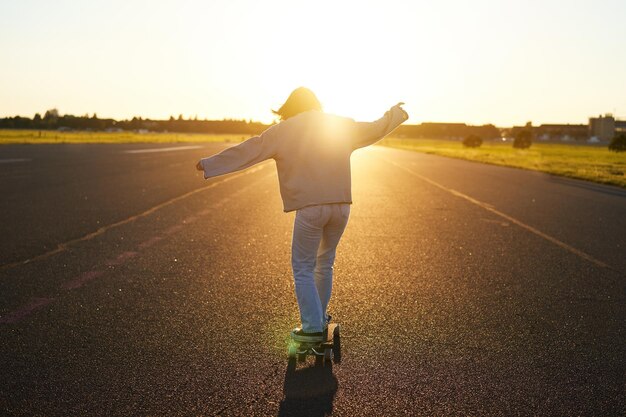 Ragazza teenager che si sente felice sul longboard felice giovane pattinatore in sella al suo skateboard con le mani distese sul lato