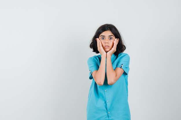 Ragazza teenager che stringe il viso con le mani in camicia blu e sembra spaventata.