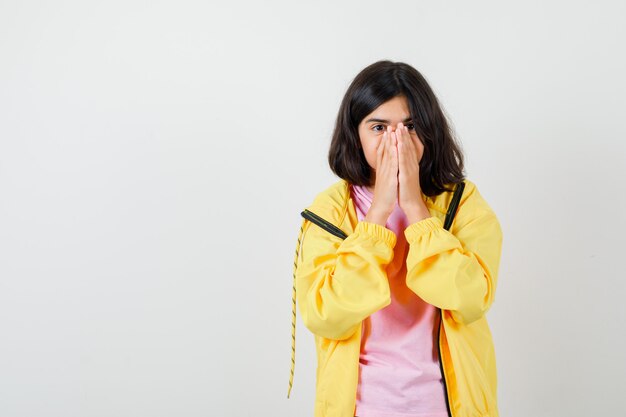 Ragazza teenager che tiene le mani sul viso in maglietta, giacca e sembra speranzosa. vista frontale.