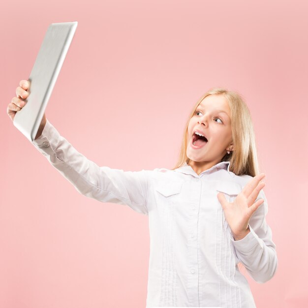 Ragazza teenager con il computer portatile. Amore al concetto di computer. Ritratto frontale a mezzo busto femminile attraente, backgroud rosa alla moda dello studio. Emozioni umane, concetto di espressione facciale.