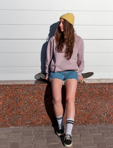 Ragazza teenager del colpo pieno che si siede sullo skateboard