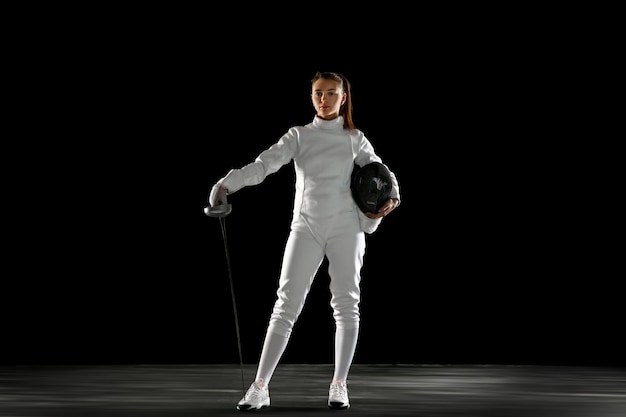 Ragazza teenager in costume da scherma con la spada in mano isolata sul nero