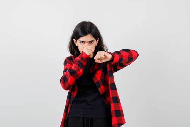 Ragazza teenager in maglietta, camicia a quadretti che sta nella posa di lotta e che sembra sicura di sé, vista frontale.