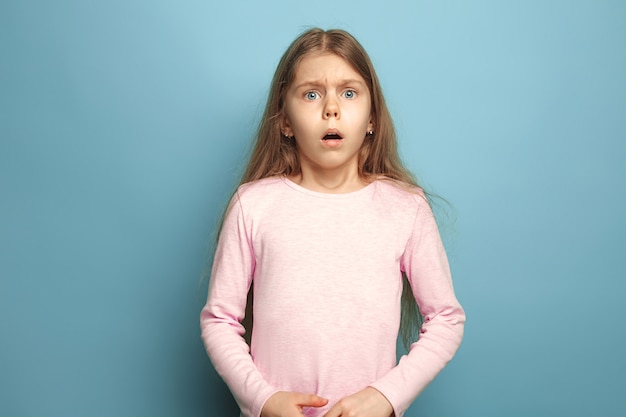 ragazza teenager sorpresa su sfondo blu studio. Le espressioni facciali e le emozioni delle persone concetto. Colori alla moda.