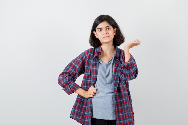 Ragazza teenager sveglia che finge di tenere qualcosa in camicia a quadri e sembra sicura. vista frontale.