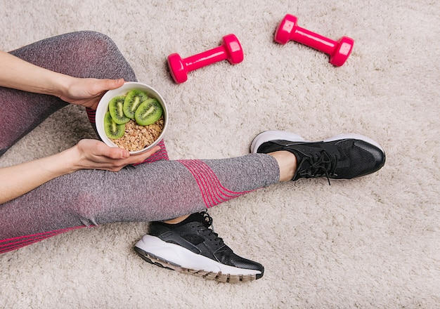 ragazza tiene un piatto con muesli e kiwi dopo allenamento fitness con manubri