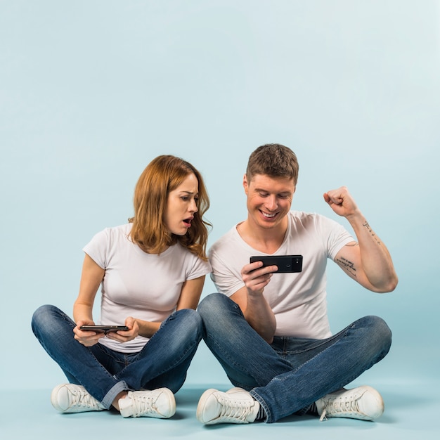 Ragazza triste che guarda il cellulare del suo fidanzato che flette i suoi muscoli