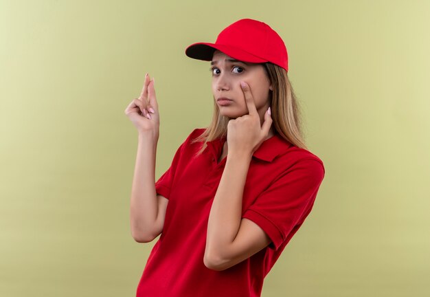 Ragazza triste di consegna giovane che indossa l'uniforme rossa e cappuccio che mostra verde isolato gesto di punta