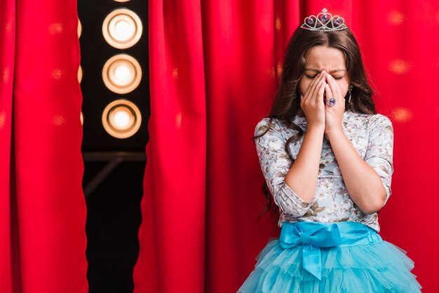 Ragazza triste in piedi dietro la tenda rossa