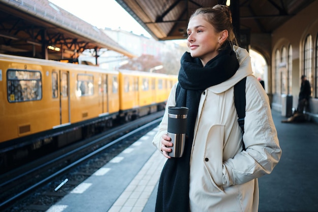 Ragazza turistica abbastanza casual felicemente in piedi sulla piattaforma in attesa del treno nella stazione della metropolitana