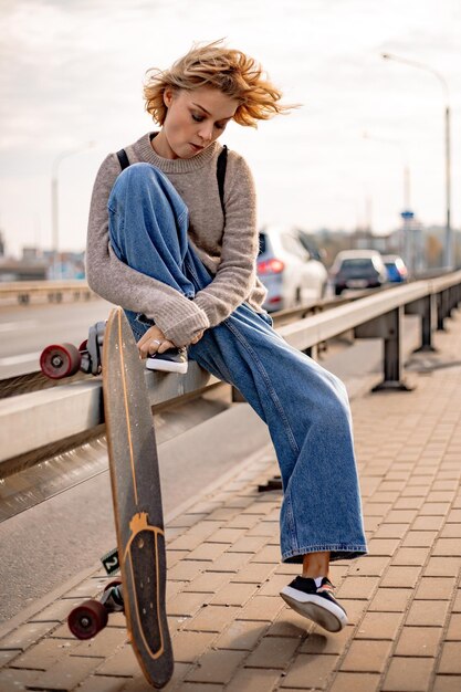 Ragazza urbana alla moda che cammina con lo skateboard. Ritratto all'aperto del modello di donna sportiva attiva. Uno stile di vita sano. Sport estremi. Look alla moda, ritratto hipster all'aperto. Close up ritratto di un grazioso