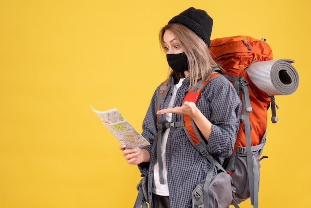 ragazza viaggiatrice con maschera nera e zaino che guarda la mappa