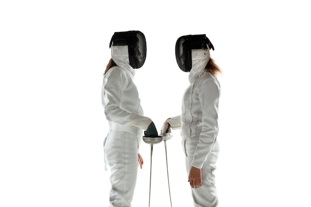 Ragazze adolescenti in costumi di scherma con le spade nelle mani isolate su sfondo bianco studio. Giovani modelli femminili formazione, posa fiducioso. Copyspace. movimento, azione.