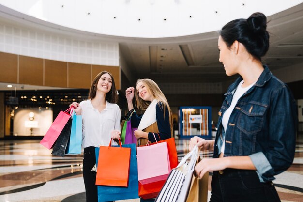 Ragazze alla moda che presentano nel centro commerciale con i sacchetti