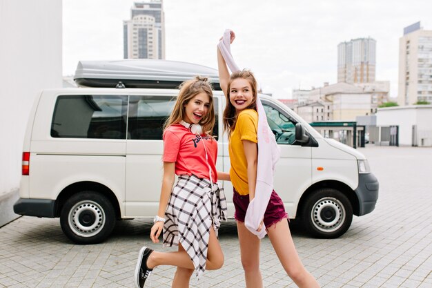 Ragazze alla moda in abiti alla moda luminosi che ballano con il sorriso, rilassandosi insieme all'aperto